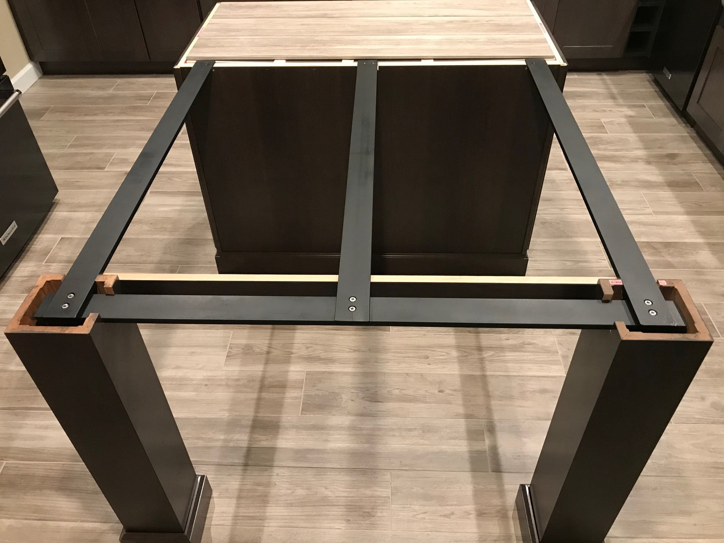 
                  
                    Squared-off Black Custom Support Brackets attached to a kitchen island with black column legs on a wooden floor.
                  
                