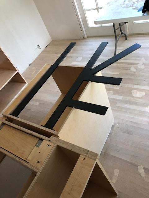 Top-down angle of Black Custom Support Brackets sitting on an unfinished wooden countertop with a white work table in the background.